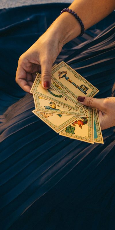 A woman holding tarot cards for a spiritual reading, set against a dark fabric backdrop.