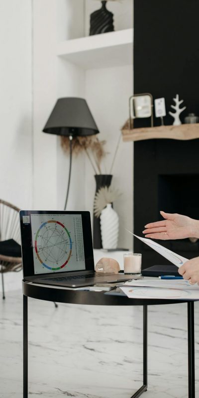 Astrologer and young woman discussing a natal chart on a laptop indoors.