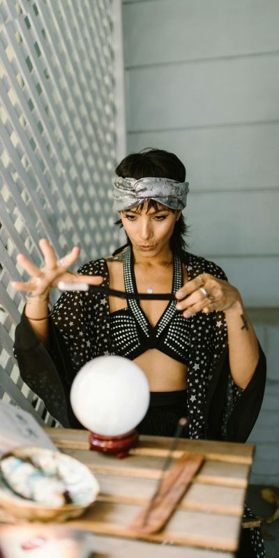 Mystical woman in patterned attire performing a ritual with crystal ball indoors.