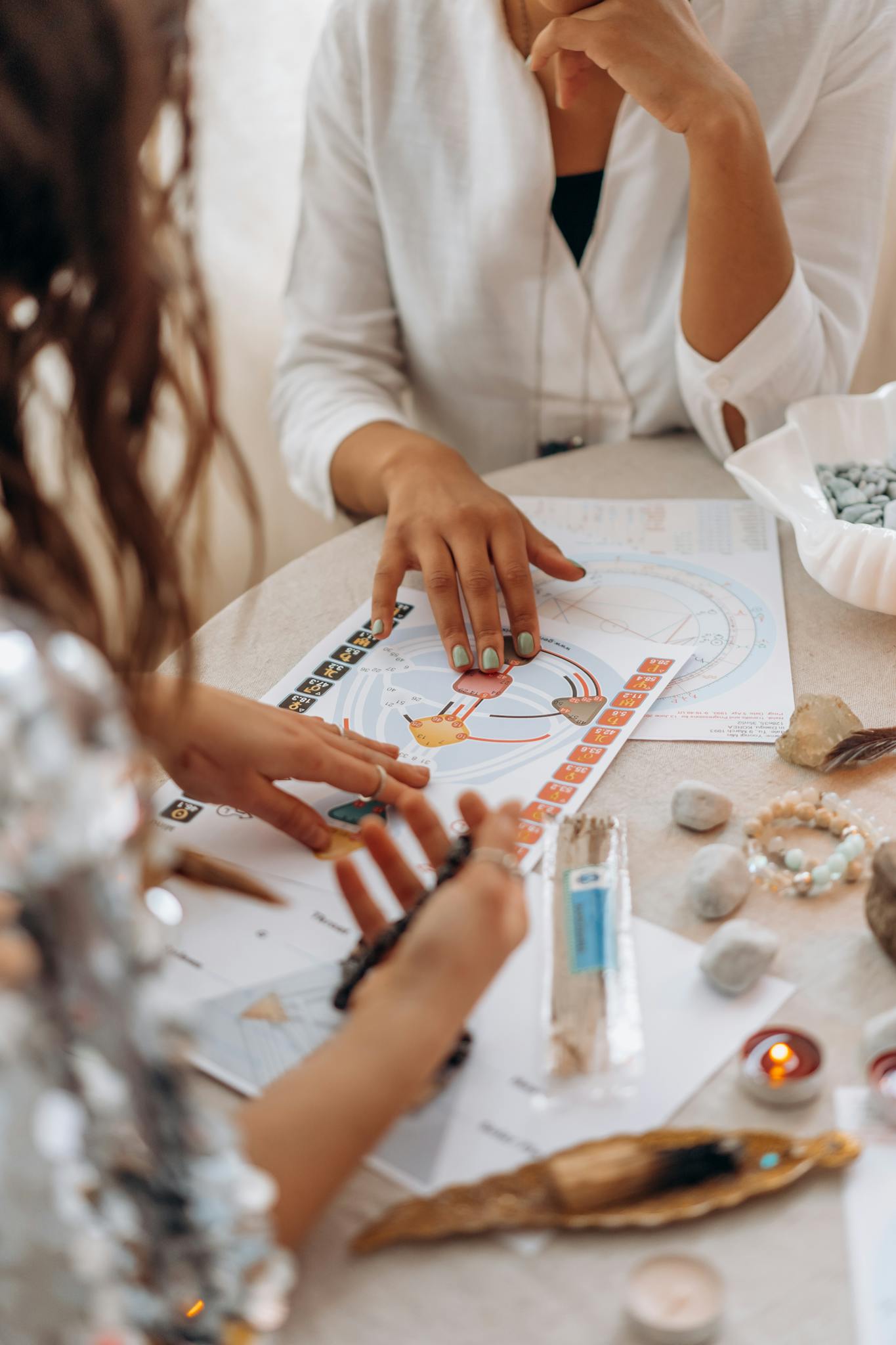 Two women exploring astrology and tarot readings at a table with stones and candles.